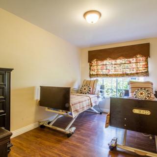 A cozy bedroom featuring hospital beds, wooden flooring, and a window with curtains.