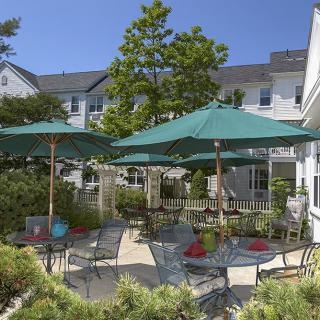A sunny outdoor patio with tables and chairs under large umbrellas, surrounded by greenery.