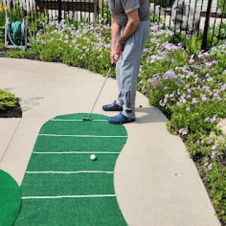 A person practicing their putting skills on a green mat surrounded by flowers.