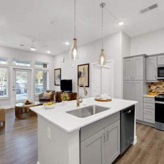 A modern open-concept kitchen and living area with sleek design elements, featuring an island counter, pendant lights, and hardwood flooring.