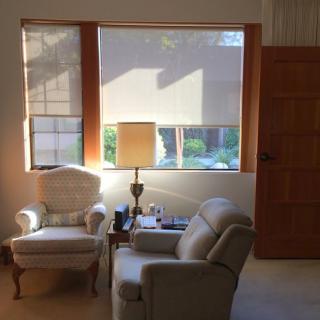 A cozy living room setup with two armchairs and a lamp by the window, illuminated by natural sunlight.