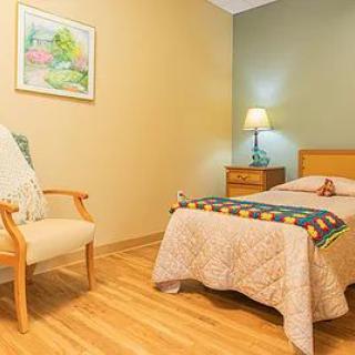 A cozy bedroom with a single bed, lamp, and wooden floor.