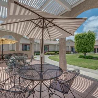 A sunny outdoor patio with tables and chairs under umbrellas, surrounded by a well-maintained garden.