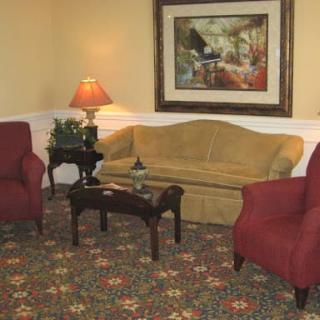 A cozy living room with a sofa, two armchairs, a coffee table, and a lamp, adorned by a painting on the wall.