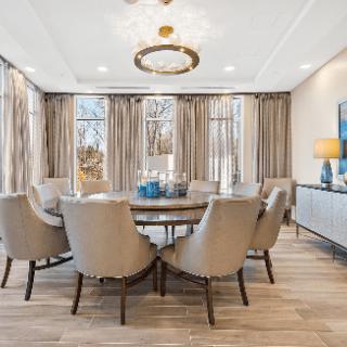 A modern dining room with a round table, upholstered chairs, and an elegant chandelier.