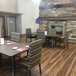 A cozy dining area with tables and chairs, featuring a stone fireplace and wooden flooring.