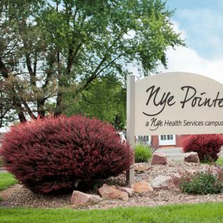 A landscaped area with a sign for Nye Pointe, featuring bushes and trees.