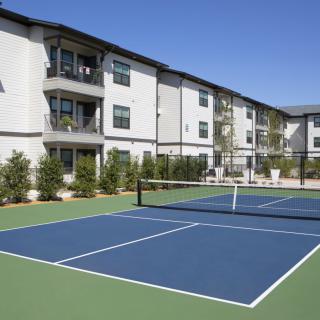 Outdoor tennis court in front of a modern apartment complex.