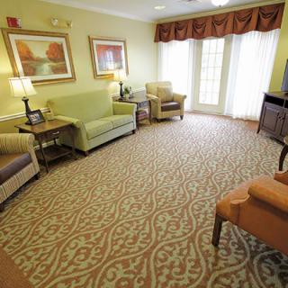 A cozy living room with sofas and armchairs arranged around a patterned carpet, adorned with paintings and ambient lighting.