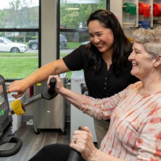 An elderly woman engaging in physical therapy with the assistance of a healthcare professional.