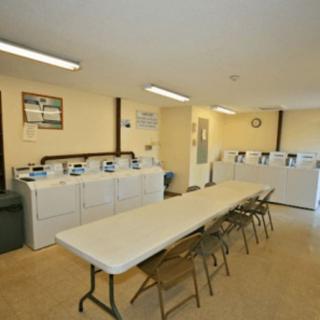 A laundry room with washing machines, dryers, and a long folding table with chairs.