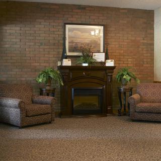A cozy living room with armchairs and a fireplace against a brick wall.