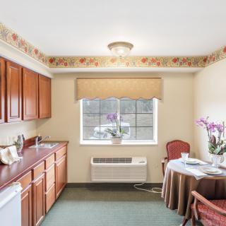 A cozy kitchen area with wooden cabinets, a small table and chairs, a window with flowers, and a neutral color palette.