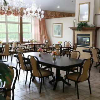 A well-lit dining area with neatly arranged tables and chairs, featuring a chandelier and a fireplace.