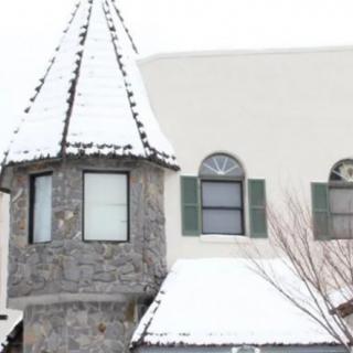 A snow-covered house featuring a tower design with arched windows.