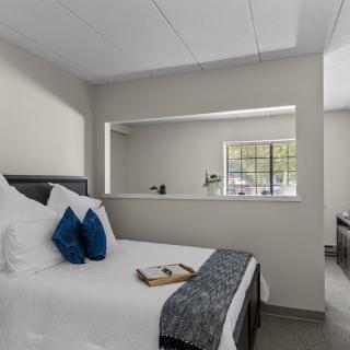 A modern bedroom with a neatly made bed and decorative pillows, featuring a window and a neutral color scheme.