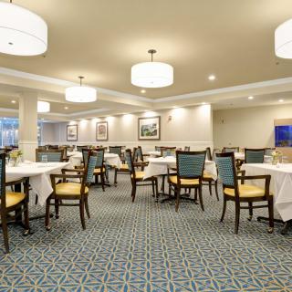 Elegant dining room with neatly arranged tables and chairs, featuring soft lighting and a carpeted floor.