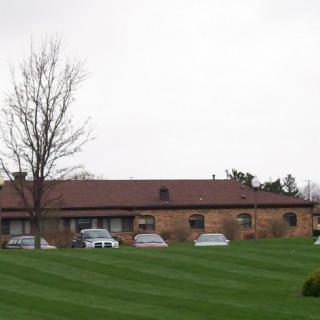 A suburban building with parked cars and a well-maintained lawn under an overcast sky.