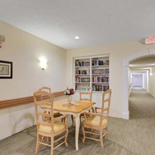 A well-lit room featuring a wooden table with chairs, a bookshelf, and an adjacent hallway.