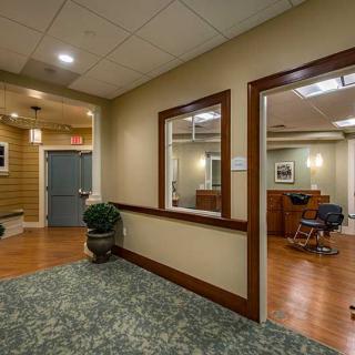 A cozy interior space with a waiting area and salon, featuring wooden floors, carpet, and potted plants.