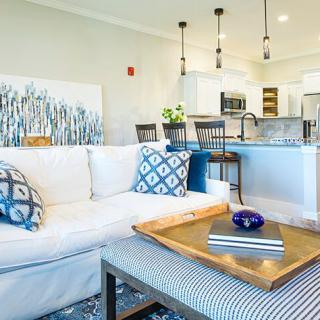A modern living room with a white sofa, patterned cushions, and a view into an open kitchen area.