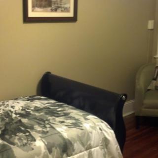 A cozy bedroom with a bed and chair, featuring wall art.