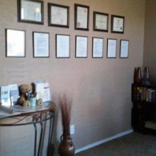 A neatly arranged wall display of framed certificates and awards in an office setting.