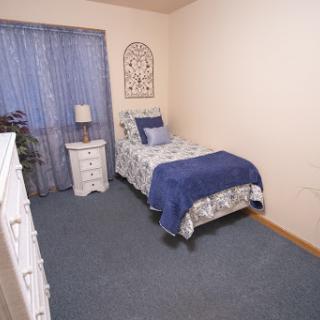 A cozy bedroom featuring a single bed adorned with blue bedding, complemented by a nightstand and curtains.