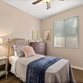 A cozy bedroom with a single bed, decorated with pillows and a throw blanket, featuring a dresser and a window with blinds.