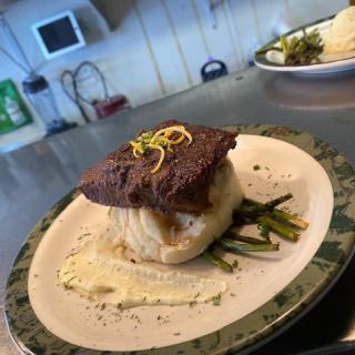 A gourmet dish featuring a piece of meat on a bed of vegetables, garnished with lemon zest.