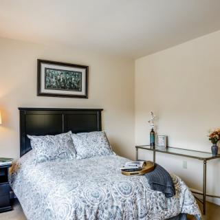 A cozy bedroom featuring a neatly made bed with patterned bedding, a nightstand with a lamp, and a desk against the wall.