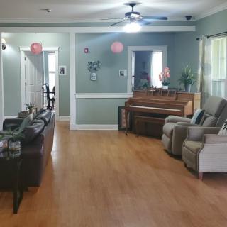 A cozy living room with a piano and comfortable seating, featuring hardwood floors and a ceiling fan.