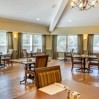 A spacious dining area with elegantly arranged tables and chairs, featuring large windows and a chandelier.