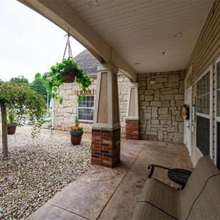A cozy covered porch with stone walls, outdoor seating, and lush greenery.