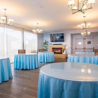 A well-decorated event room with round tables covered in blue tablecloths and elegant chandeliers.