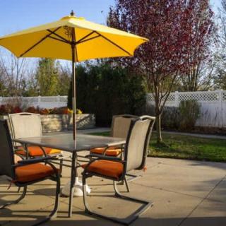 A sunny backyard patio with a table, chairs, and a yellow umbrella.