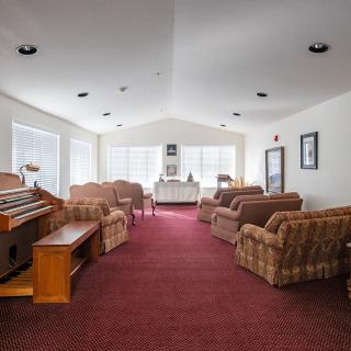 A spacious living room with a carpeted floor, sofas, and ample natural light streaming through large windows.