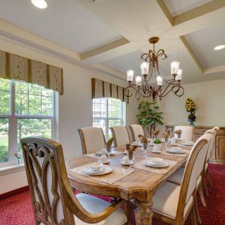 An elegant dining room featuring a large wooden table set for a meal, illuminated by a chandelier and surrounded by large windows.
