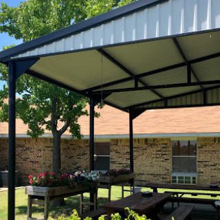 A sunny outdoor pavilion providing shade for a picnic area, surrounded by lush greenery.