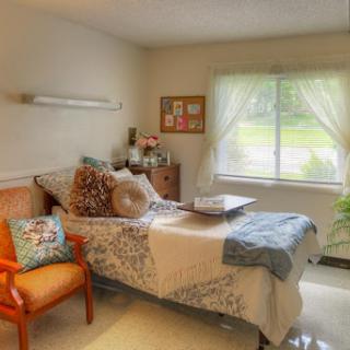 A cozy and well-lit bedroom with soft decor, featuring a comfortable bed and an inviting chair.