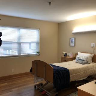 A well-lit hospital patient room featuring a neatly made bed and a window.