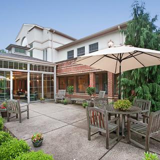 A spacious patio with wooden furniture and an umbrella, surrounded by greenery.