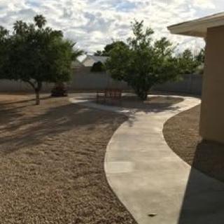 A backyard with a curved paved path, trees, and a cloudy sky.