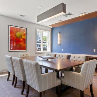 A modern dining room with a large table, upholstered chairs, and colorful artwork on the wall.