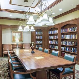 A well-lit conference room with a large wooden table surrounded by chairs, flanked by bookshelves filled with books.
