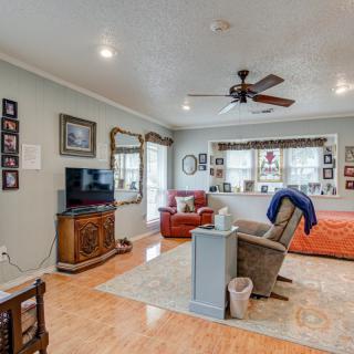 A cozy living room with a comfortable arrangement of furniture, including a sofa, chair, and television. The walls are adorned with various framed photos, and the room features hardwood flooring and a ceiling fan.