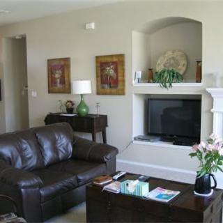 A cozy living room featuring a leather sofa, a TV mounted above a fireplace, and tasteful decor including plants and artwork.