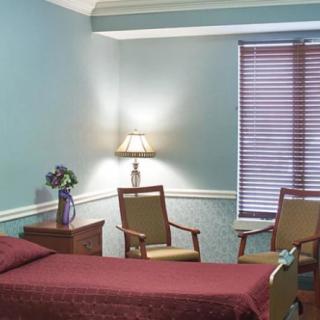 A cozy room with a bed, two chairs, and a lamp near the window.