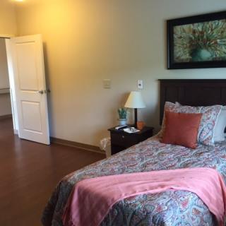 A cozy bedroom featuring a single bed with colorful bedding, a bedside lamp, and artwork on the wall.
