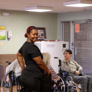 A healthcare worker smiles while attending to elderly patients in a nursing home.